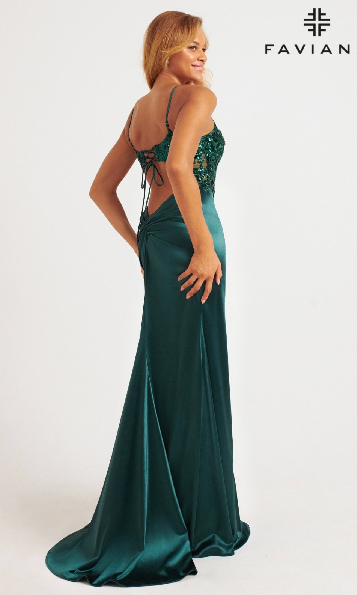 A woman poses in the Faviana 11200, a floor-length emerald green prom dress with sequin bodice, lace-up back, fitted silhouette, and a slight train. The brand name